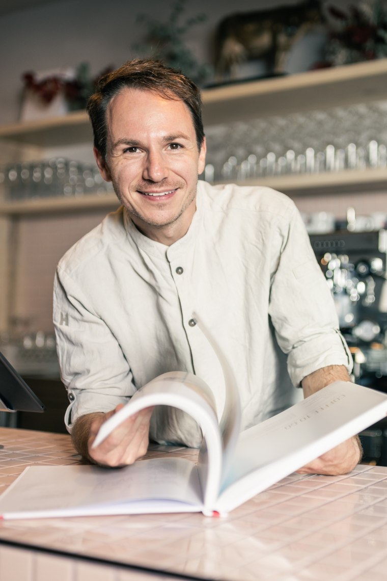 Matthias Krenn blättert in seiner Feinbäckerei hinter der Theke in seinem Buch