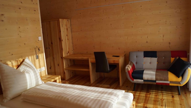 Holzvertäfeltes Zimmer mit Bett, Schreibtisch und bunter Couch., © Fam. Exenberger