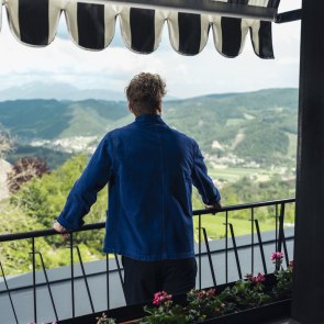 Ein Mann steht auf einem Balkon und blickt in die Landschaft.