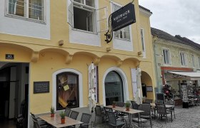 Gelbes Gebäude mit Bar 'Kalmuck', Außentische auf Kopfsteinpflaster., © Donau NÖ Tourismus