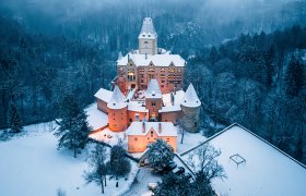 beleuchtete Burg bei Nacht auf Hügel mit schneebedeckter Landschaft