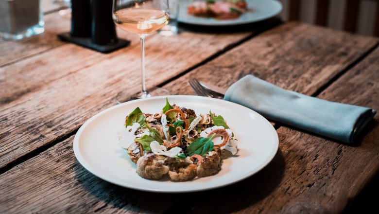 Gourmetgericht auf rustikalem Holztisch mit Weinglas und Besteck., © test