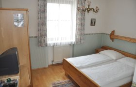 Gemütliches Schlafzimmer mit Holzmöbeln und TV, helle Fensterdekoration., © Gh Grubmüller