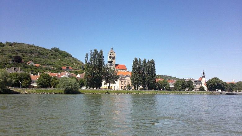 Stadtansicht mit Kirche und Hügeln am Flussufer, blauer Himmel., © Donau NÖ Tourismus BF