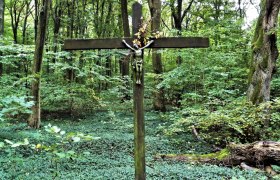 Holzkreuz mit Christusfigur in einem dichten, grünen Wald., © Donau Niederösterreich