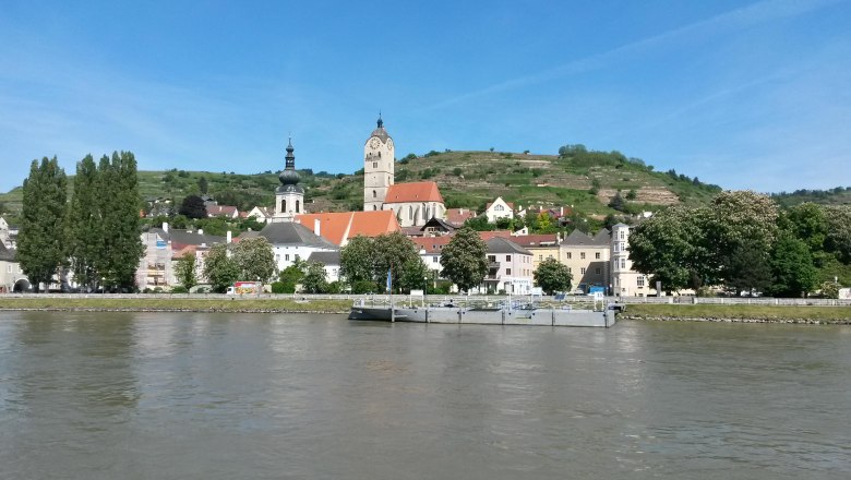 Stadtansicht mit Kirche und Hügeln am Flussufer, blauer Himmel., © Donau NÖ Tourismus BF