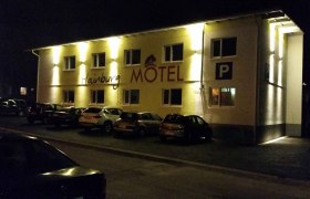 Beleuchtetes Motelgebäude bei Nacht mit geparkten Autos davor., © hainburg motel