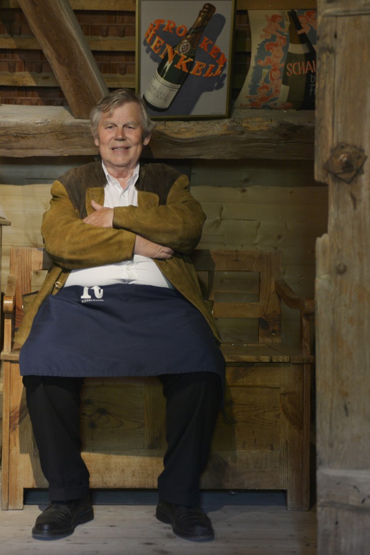 Älterer Mann sitzt auf einem Stuhl aus Holz in einem Haus aus Holz.