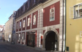 Historisches Gebäude mit roter Fassade und Torbogen in einer Altstadtstraße., © Mondseer Stiftshof