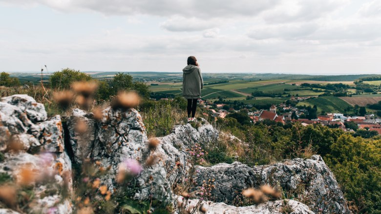 Frau steht auf einem steinigen Hügel und blickt in ein Dorf hinunter