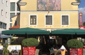 Gelbes Gebäude mit Wandgemälde, Café mit grünen Sonnenschirmen., © Donau NÖ Tourismus GmbH