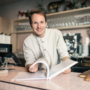 Matthias Krenn blättert in seiner Feinbäckerei hinter der Theke in seinem Buch