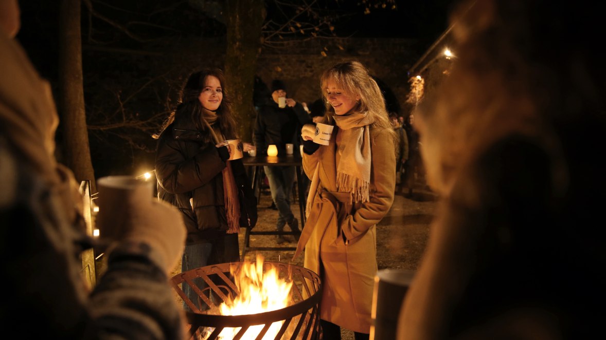 Zwei Frauen trinken Punsch bei einem Feuer